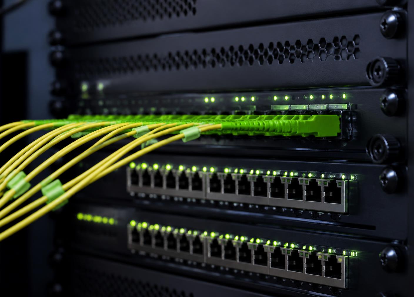 Close-up of network switches and fibre optic patch cables with green port indicators